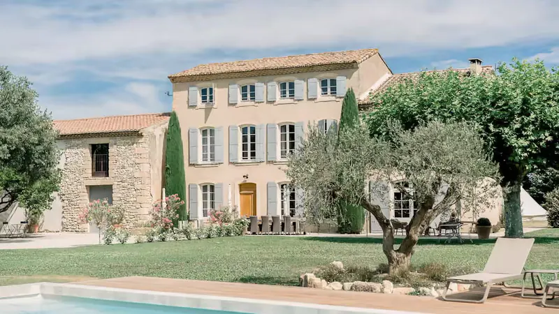 The pale stone facade and blue shutters of La Bastide des Barattes, seen from the lawn beside the pool