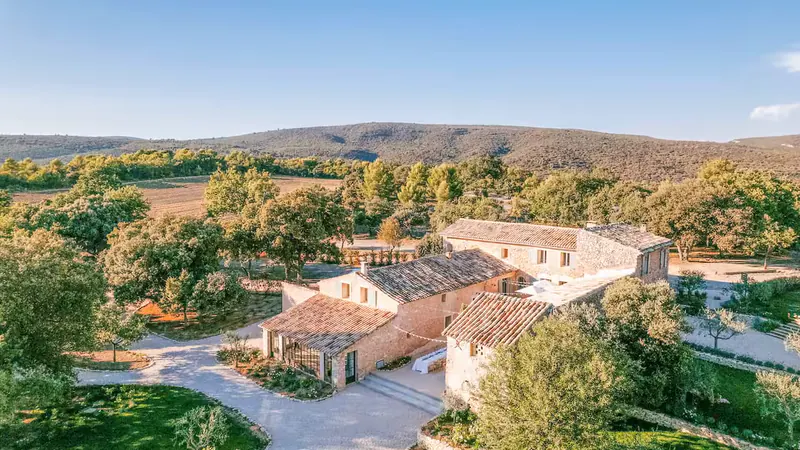 Aerial view of the stone buildings of Le Mas de Florette at golden hour, the Luberon hills behind